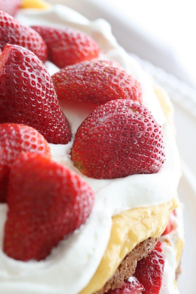 Grain free and gluten free coconut cake topped with honey-sweetened lemon curd, strawberries and billows of whipped cream.